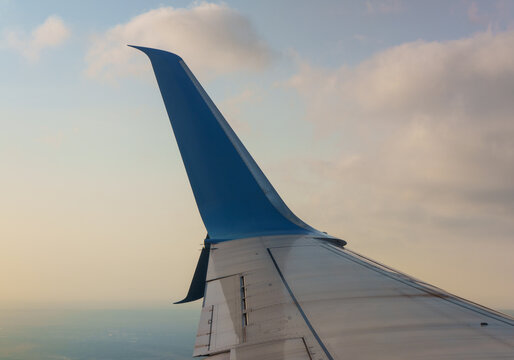 Passenger airplane aircraft wing with blue winglet flying high above the earth ground during a scenic sunset evening sky. Modern commercial aviation transport vehicle, summer vacation journey. 