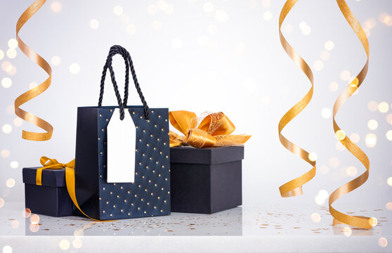 Elegant black gift boxes and shopping bag with gold ribbons in bokeh lights