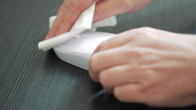 Person cleaning white computer mouse with tissue on dark wood surface