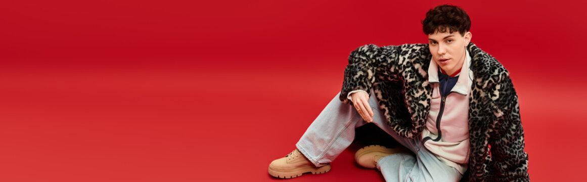 Young man showcases stylish fashion against vibrant red background