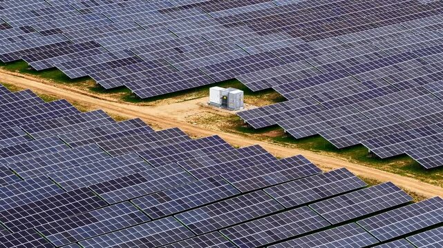 Aerial view of rows of photovoltaic solar panels and a small electrical substation in a rural field in Latvia.