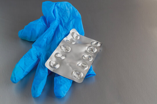 Used blue medical glove with an empty blister pack for pills on a grey surface.