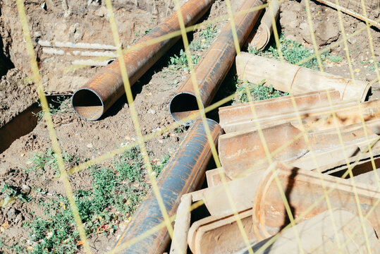 A construction site features yellow safety netting surrounding drainage pipes lying on the ground within a trench
