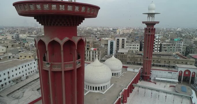 Aerial view of a mosque with white domes and a tall red minaret overlooking the dense urban landscape of old city area Karachi, Sindh, Pakistan.