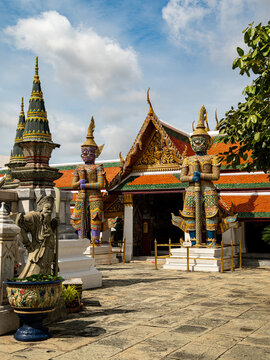 View of The Temple of the Emerald Buddha featuring ornate demon statues and traditional Thai architecture in a stone courtyard in Krung Thep Maha Nakho, Thailand.