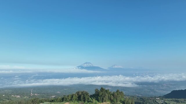 Aerial view of Menoreh mountains rising above a sea of clouds under a clear blue sky in Salaman, Central Java, Indonesia.