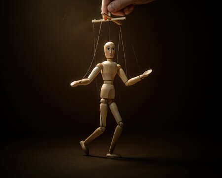 Wooden marionette puppet controlled by strings held by a human hand