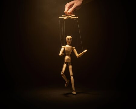 Wooden marionette puppet controlled by a human hand, dark background