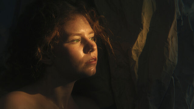 Red Haired Woman Retreats Behind Fragile Paper Barrier, Creating Metaphor For Self Protection and Feeling Exposed. Cinematic Shadows and Warm Light Convey Vulnerability and Emotional Openness.