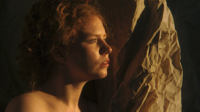 Woman Surrounded by Crumpled Paper Pauses in Private Inner World, Reflecting on Thoughts and Emotions. Warm Cinematic Light and Deep Shadows Create an Intimate Visual Metaphor For Self Discovery.