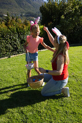 Mom and daughter kneeling in garden wearing bunny ears with baskets and eggs mom's smartwatch © WavebreakMediaMicro