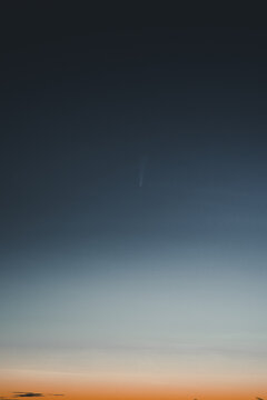 View of Comet Neowise in the night sky with a gradient from dark blue to orange at the horizon in Merikula, Harju maakond, Estonia.