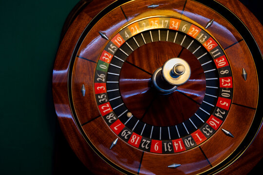 Casino roulette wheel with white ball stopped near red number 7. Classic gambling device highlights lucky seven slot on rim. Polished wooden gaming equipment captures betting action.