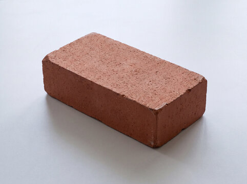 Single red clay brick on a light gray surface
