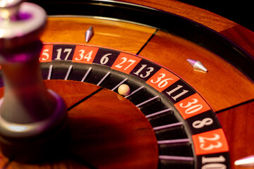 Casino roulette wheel with white ball stopped on black number 13 slot. Wooden gambling device features metal turret in close view. Macro photography captures betting game action. © Mati