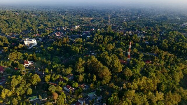Aerial view of Kaliurang with dense forest, scattered buildings, and a communication tower in Pakem, Special Region of Yogyakarta, Indonesia.