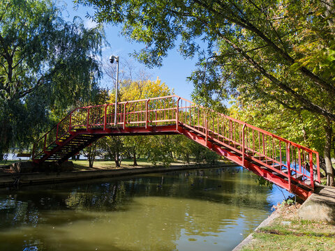 Red Pedestrian Bridge Over a Park Lake Surrounded by Green Trees