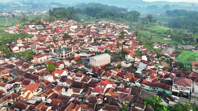 Aerial view of the village of Ciwidey with red-tiled rooftops nestled among lush green hills and rice fields in Bandung, West Java, Indonesia.