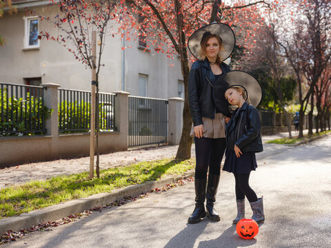Mother and daughter go trick or treating down residential street during Halloween. Family holds pumpkin lanterns passing decorated autumn houses in Zagreb Croatia