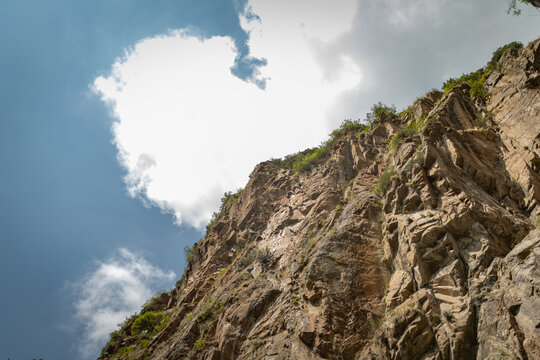 Majestic rocky canyon cliff with sparse green vegetation rising against a blue cloudy sky