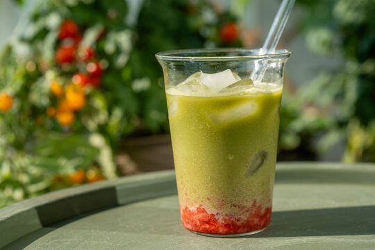 Refreshing iced strawberry matcha latte with colorful layers of fresh strawberry, milk and green matcha served outdoors in a lush summer garden