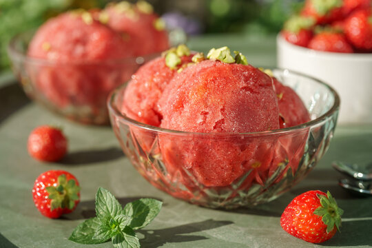 Close-up of homemade strawberry sorbet served in a glass dessert bowl with fresh strawberries and mint on a sunny summer table