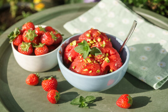 Homemade strawberry sorbet served with fresh strawberries and mint on a sunny outdoor table, showing the natural texture of a refreshing summer dessert