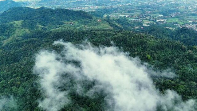 Aerial view of Bukit Sabak Sukabumi with lush green hills partially covered by mist and clouds in Sukalarang, West Java, Indonesia.