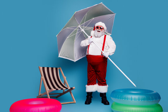 Santa Claus on summer vacation at the beach with umbrella, sunglasses and inflatable rings in a playful holiday scene