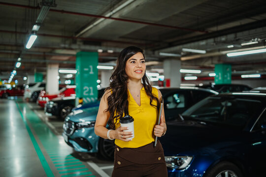 Businesswoman walking in parking garage with coffee and laptop