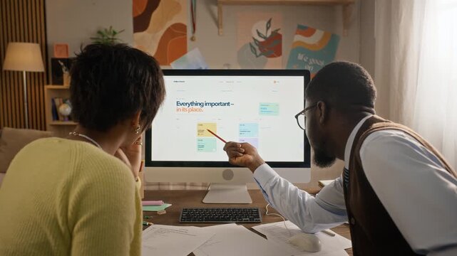 African American male tutor explaining digital schedule on desktop computer to teenage girl, rear view. Video ideal for private tutoring ads and edtech promotions