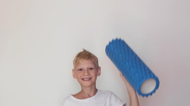 Strong healthy child and kids strength training, smiling boy in white t-shirt with blue foam roller on light background. Strong kid for sport stores and schools, boy lifts roller up like weight