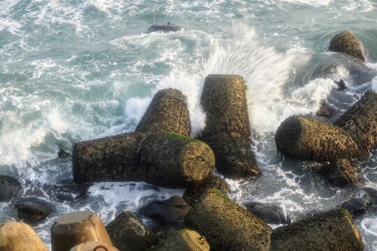 Ocean wave splash crashing against concrete tetrapod breakwater structures along the coastline.