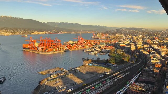 Aerial view of the Port of Vancouver at golden hour with red gantry cranes, container stacks and rail lines along Burrard Inlet below the North Shore mountains.