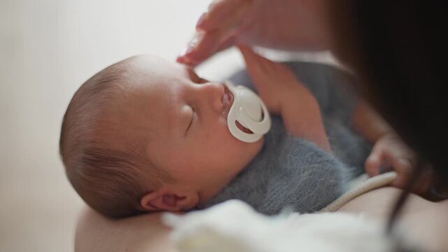 Newborn Baby Sucking A Pacifier In Its Mother's Arms