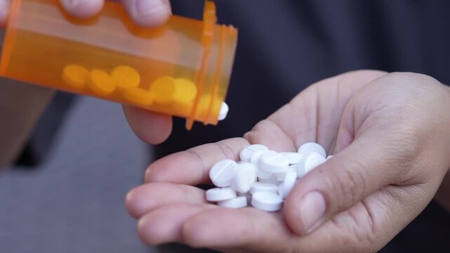 close up woman hand holding a medicine, with pours the pills out of the yellow orange medicine bottle. Stop drug use Taking Medication Caring for the health care medical concept.