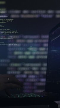 Vertical video. Hacker writing code cracking computer. Programming code in the background. Hacker attack, cybercrime, virus software, dark web, cyber security concept.