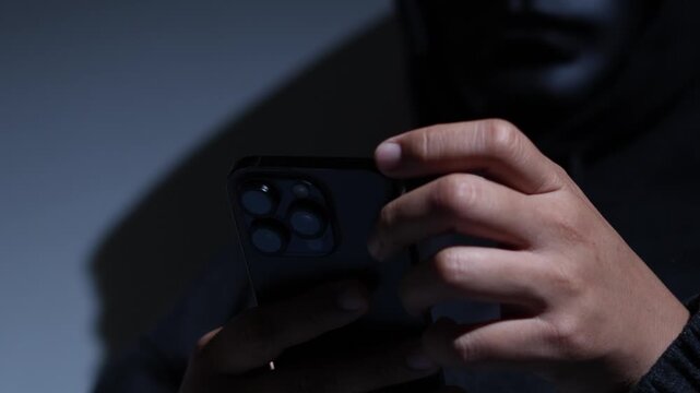 Phone scammers protection, mobile security, wearing black hood sitting in dark.