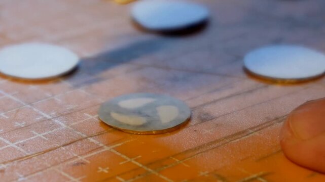 Surface cleaning of a circular metal disc with a cloth followed by fine manual scribing and pattern etching work on a structured workbench surface during preparation.