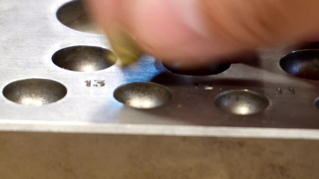Metalworking operation utilizing a heavy steel dapping block and a specialized punch tool to form flat brass discs into precise hemispherical shapes within a workshop.