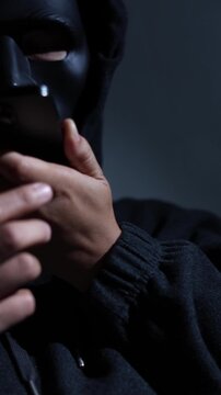 Phone scammers protection. Unknown businessman wearing mask with covered face using mobile makes an anonymous call intimidating and threatening the interlocutor on dark background. hacker call center.