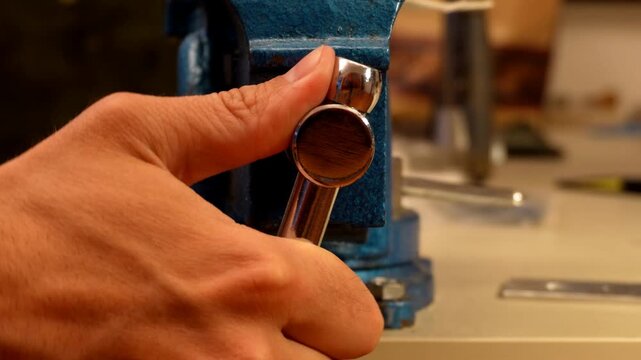 Metal vise clamping a drilled metal plate securely while a file smooths down the surface and levels a protruding brass rod during workshop operations.