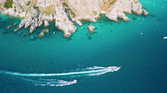 Capo Vaticano Calabria Italy 4k drone view of speedboats racing on turquoise sea. Top down view of two motorboats with white wake along rugged cliff coastline establishing shot