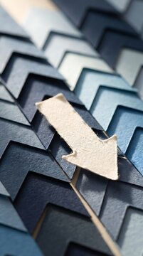 Beige paper arrow pointing down on layered blue chevron paper pattern, close up macro with shallow depth of field, direction concept, decline, business trend, paper craft background
