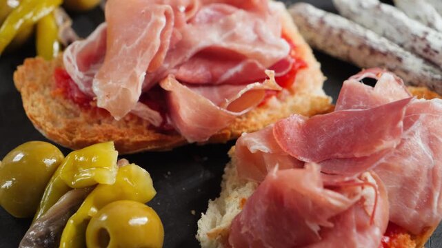 Pan con tomate topped with slices of jamon, served with pickled peppers, olives and mini fuet sausages. High quality 4k footage