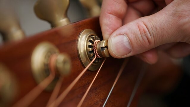 Close-up of hand adjusting tuning peg on classical acoustic guitar headstock