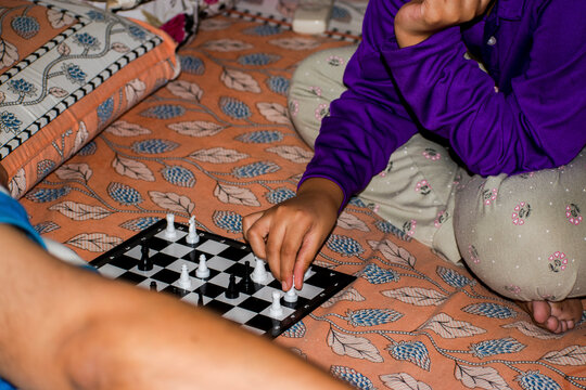 Child playing chess indoors with her father.