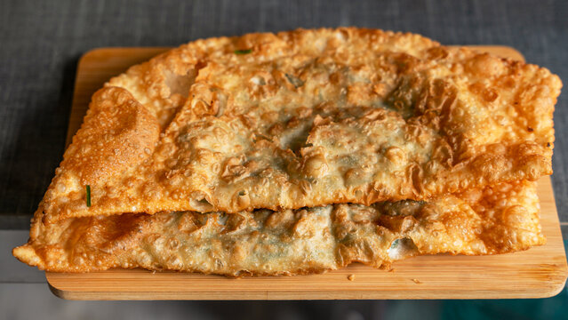Golden crispy traditional chebureki with beef and mountain leek (jusai) on wooden board. Homemade Central Asian meat pie close-up, crispy bubbled dough.
