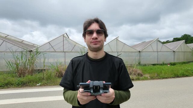 Man using a drone controller near greenhouses in Da Lat Vietnam