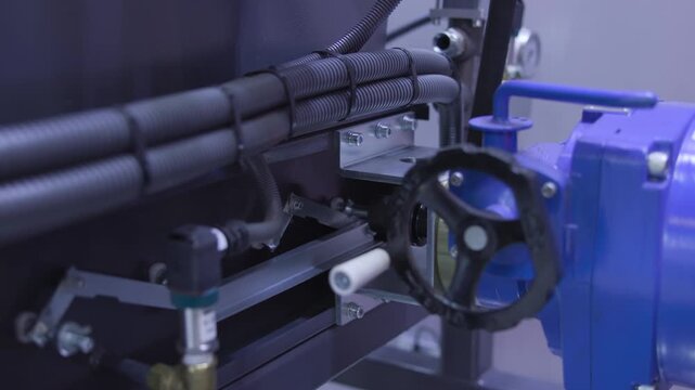 Close-up view of industrial motor housing and bundled ribbed conduits with metal bracket, bolts, and black circular handwheel in cool diffuse factory lighting detail